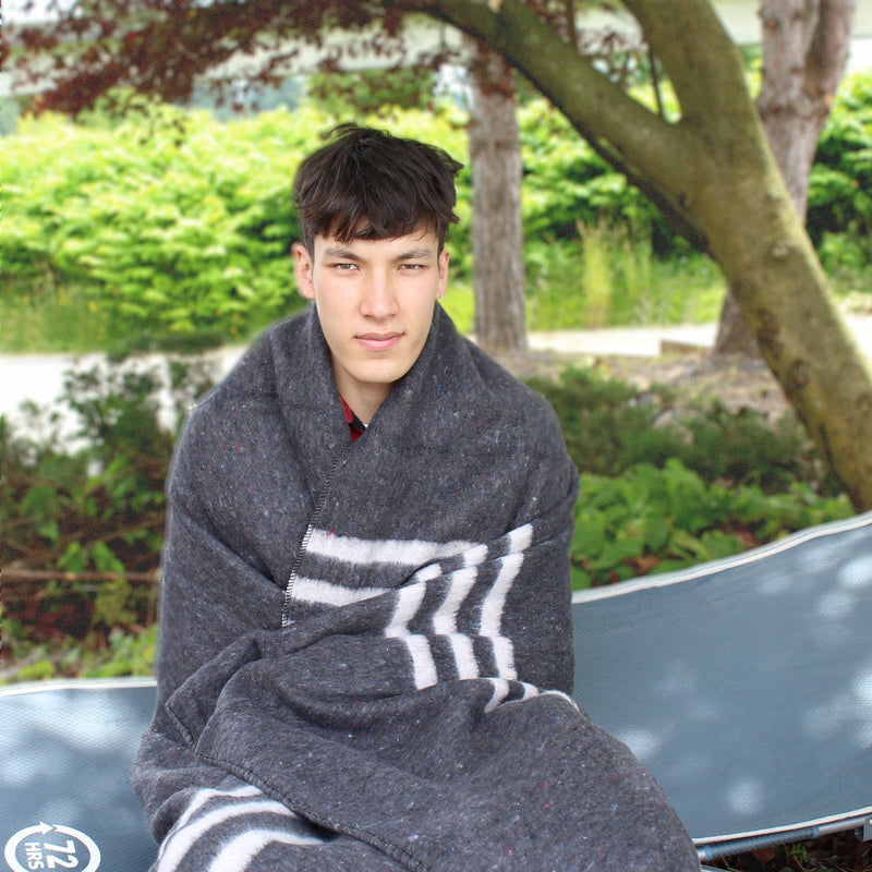 man wrapped in Gray and White Cotton Blanket outdoors sitting on camping cot