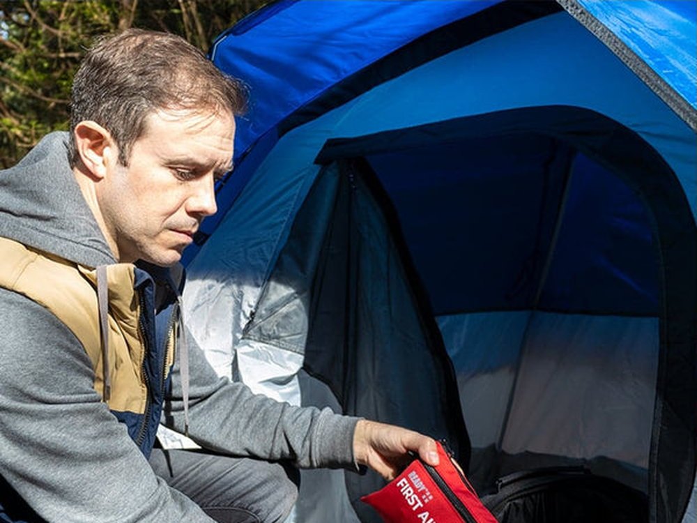 Man reaching for the Ready First Aid kit inside a camping tent