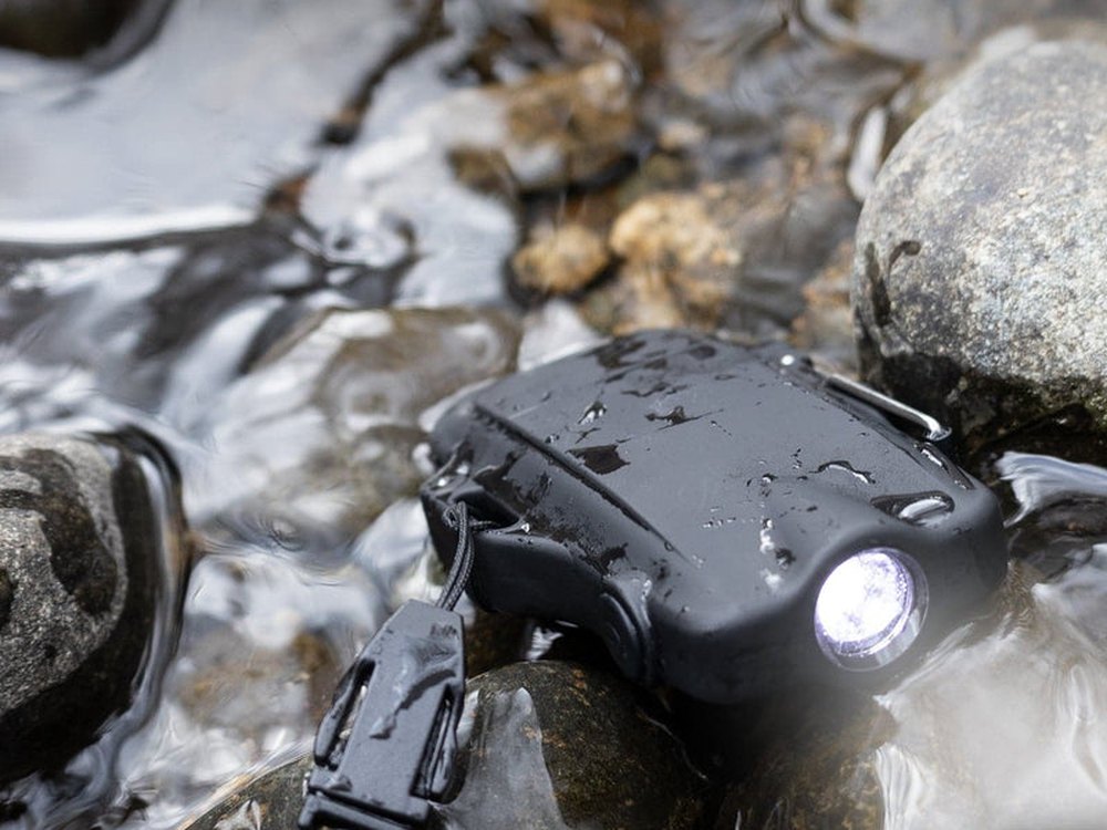 72HRS electric lighter with its flashlight on, lying on wet rocks in the rain
